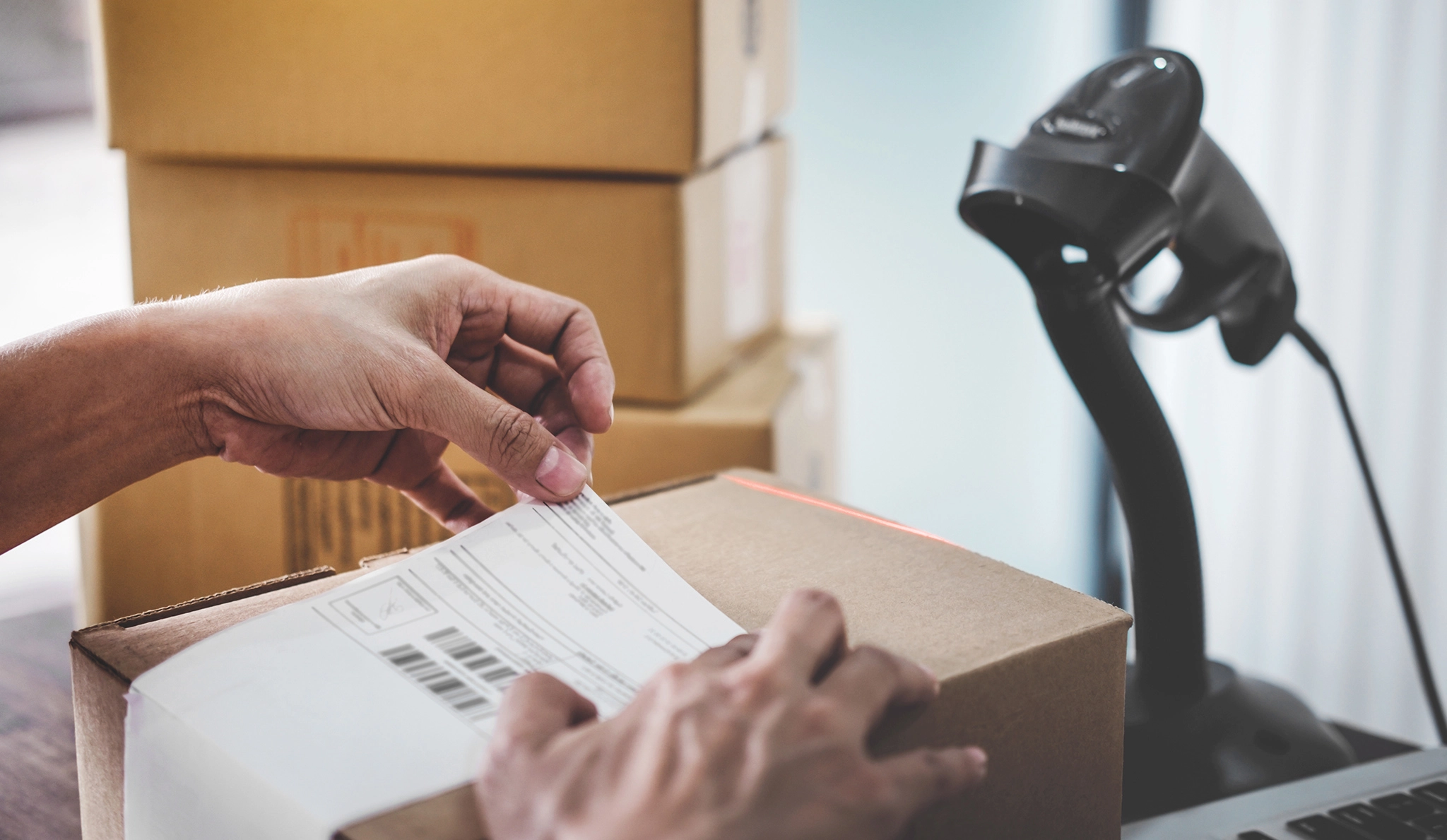 An employee is applying a shipping label to a package in front of a barcode scanner, illustrating the automation of the shipping process.