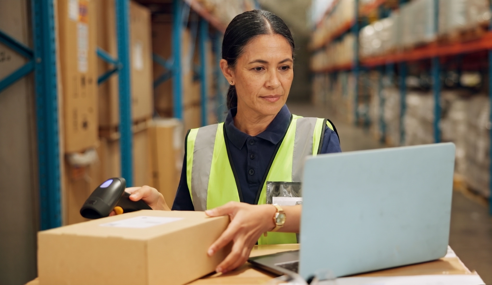A warehouse worker scans packages using a handheld scanner in a warehouse, ensuring rigorous real-time inventory tracking.