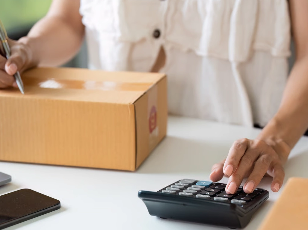 Calculating costs on a calculator while standing in front of a package, symbolizing the estimation of customs duties, taxes, and unloading fees